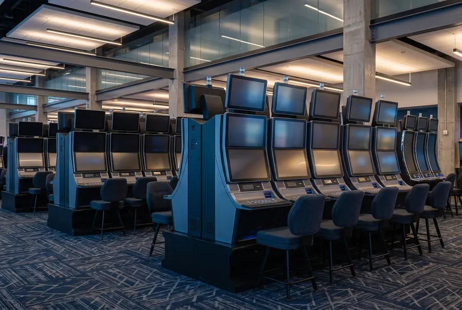 Scène générée : une rangée de machines à sous bleu acier et graphite, aux écrans de couleurs abstraites; ce n'est pas une photo du casino.